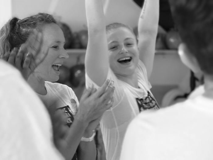 Two students laughing while another goes up into a handstand